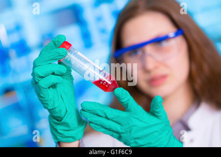 Modello rilasciato. Farmacia femmina tenendo la siringa con liquido rosso in laboratorio. Foto Stock