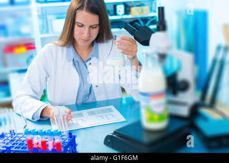 Modello rilasciato. Donna scienziato tenendo un bicchiere di vetro con il latte. Foto Stock