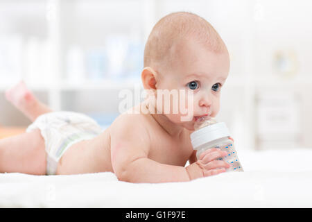 Neonato Bimbo beve acqua dalla bottiglia giacente sul letto. Bambino pannolino usurata in salotto. Foto Stock