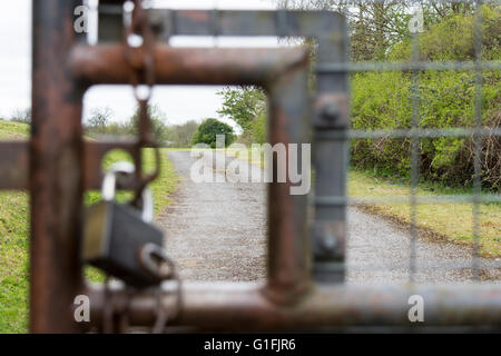 Vista del lucchetto chiuso per esterno in metallo cancelli di sicurezza con attenzione alla possibile strada per la libertà al di là di Foto Stock
