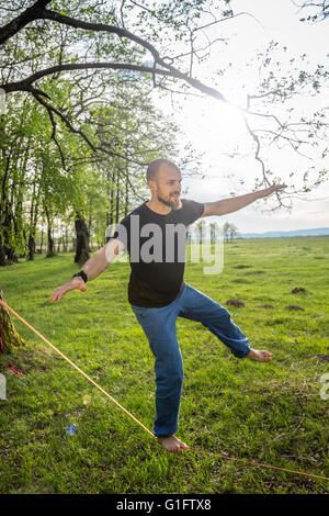 Uomo in equilibrio su slackline nella foresta Foto Stock