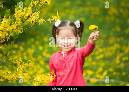Ritratto di funy bambina con il tarassaco giallo in mano. Bella sorridente bambino che gioca con i fiori sulla giornata di primavera Foto Stock