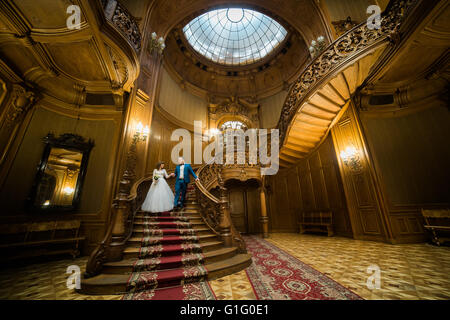 Bella coppia sposata holding hands scendendo le scale a ricchi interni in legno Foto Stock