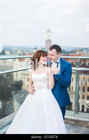 Lo sposo costeggiata da sposa indietro passando per kiss permanente sulla terrazza con grande cityscape Foto Stock