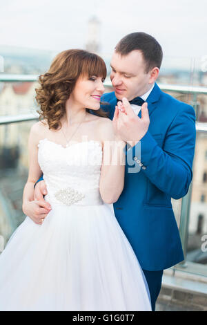 Lo sposo costeggiata da sposa indietro passando per kiss permanente sulla terrazza con grande cityscape Foto Stock