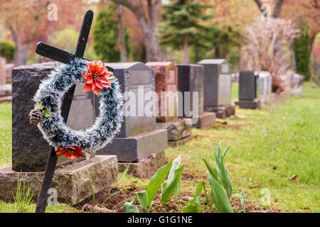 Funerale corona con fiori di colore rosso su una croce in un cimitero, con molte lapidi in background. Foto Stock