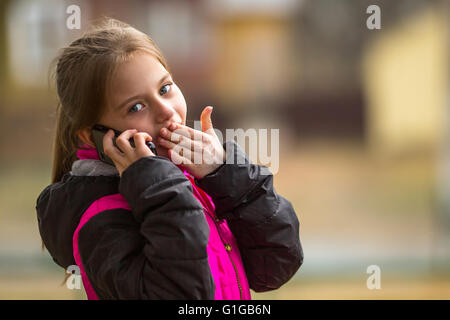 Poco carino ragazza parlando al telefono in strada. Foto Stock