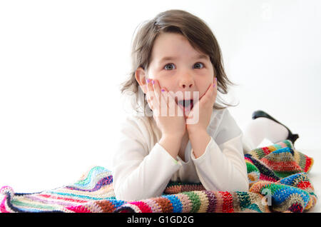 Ragazza dolce stupito sedersi sulla coperta colorata isolato su bianco Foto Stock