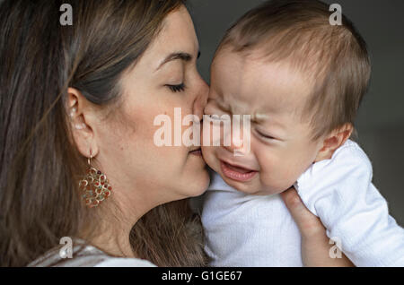 Giovane madre cercando di comfort e di calmare il suo pianto baby boy. Foto Stock