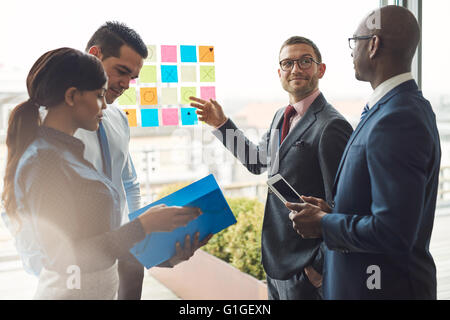 Gruppo di giovani di diverse persone di affari nella riunione della conferenza utilizzando colorato note adesive per organizzare le idee sulla grande finestra in vetro Foto Stock