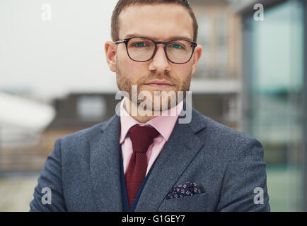 Imprenditore pensieroso fissando attentamente la macchina fotografica con un grave espressione imperscrutabile, close up tagliato di testa e spalle Foto Stock