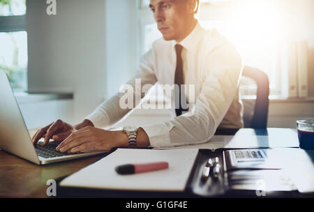 Business uomo al lavoro su un notebook in ufficio con i documenti sulla sua scrivania, indossa una tuta e tirante Foto Stock