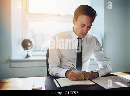 Executive business uomo che lavora in ufficio la scrittura in un calendario e cercando seriamente Foto Stock