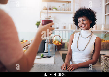 Juice bar proprietario con il cliente femmina con in mano un bicchiere di succo di frutta fresco. Donna africana in piedi dietro il bancone e sorridente. Foto Stock