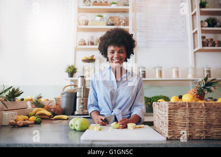 Ritratto di giovane e bella donna africana in piedi dietro il bancone bar e trinciatura di frutta fresca. La donna lavora al bar dei succhi. Foto Stock