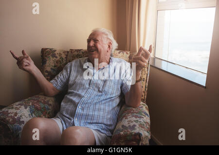 Piscina colpo di felice vecchio seduto su una sedia di braccio e sorridente. Uomo Senior in un momento di relax a casa per anziani. Foto Stock