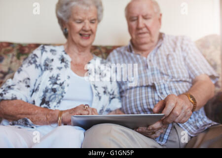 Ritratto di felice coppia senior seduti insieme a casa e con tavoletta digitale. Anziani uomo e donna seduta su un divano con t Foto Stock