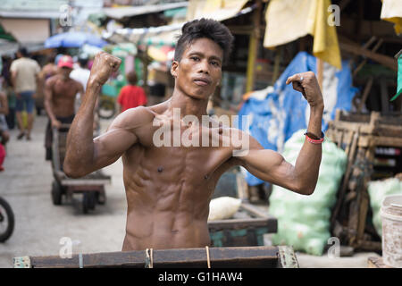 Un giovane uomo filippino lavorando all' interno del mercato del carbonio Cebu City,Filippine visualizza il suo telaio muscolare. Foto Stock