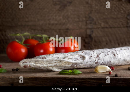 Salame con le spezie e le verdure sopra rustico sfondo di legno Foto Stock