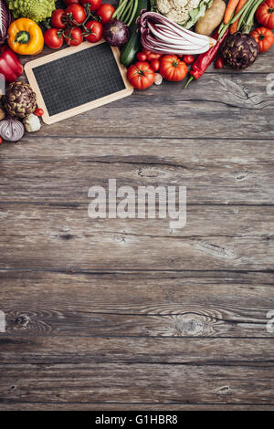 Fresche verdure organiche composizione con lavagna vuota su una tavola in legno rustico, mangiare sano e cibo vegetariano concept Foto Stock