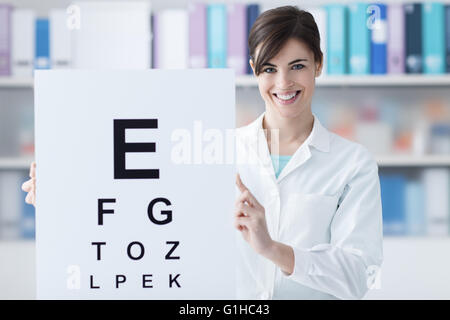 Femmina oculista professionale tenendo un occhio grafico e sorridente alla fotocamera, visita medica e cure oculistiche concept Foto Stock