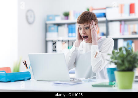 Scioccato donna con testa in mani avendo problemi con il computer, è lei a urlare e a fissare lo schermo del laptop Foto Stock