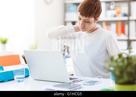 Lavoratore di ufficio seduti alla scrivania e toccando il suo indietro, sta avendo un dolore al collo Foto Stock