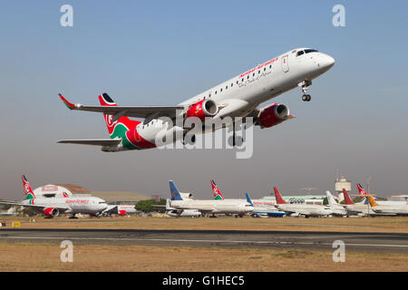 Un jet regionale Embraer E190 della Kenya Airways decolla dalla pista all'aeroporto Jomo Kenyatta di Nairobi, Kenya. Aerei in disuso e immagazzinati visti dietro Foto Stock