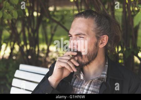 Barbuto uomo asiatico di fumare il sigaro in estate park, outdoor ritratto con il fuoco selettivo Foto Stock