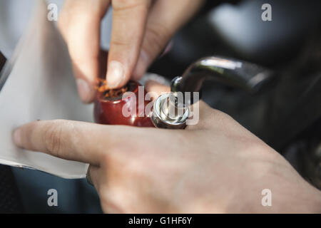 L'uomo riempie il tubo con il tabacco, vicino la foto con il fuoco selettivo sul tubo Foto Stock