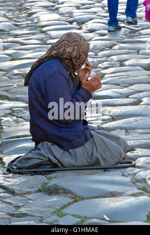 Una donna senzatetto per le strade di Roma in ginocchio sul terreno mentre Pregando e chiedendo soldi Foto Stock