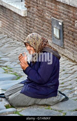 Una donna senzatetto per le strade di Roma in ginocchio sul terreno mentre Pregando e chiedendo soldi Foto Stock