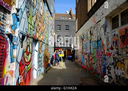 Turistico con bagaglio stop fro una pausa in un coperto di graffiti vicolo nella zona est di Londra Foto Stock