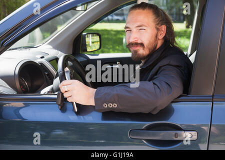 Barbuto uomo asiatico con i tasti come un driver di moderni SUV giapponesi, outdoor ritratto in aprire la finestra auto Foto Stock