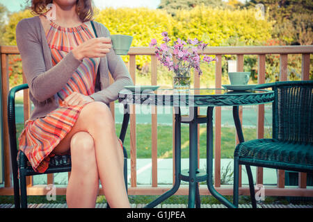 Una giovane donna è seduta e di bere il tè sulla terrazza in estate Foto Stock