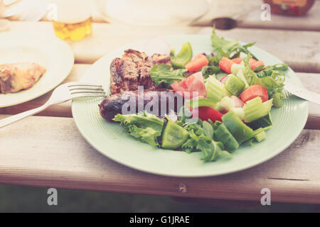 Una piastra con insalata di fresco e carne alla brace su un tavolo fuori in una giornata di sole Foto Stock