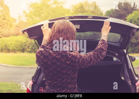 Una giovane donna è l'apertura del tronco di un automobile Foto Stock