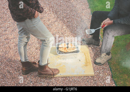 Due persone sono in piedi intorno a un barbecue monouso al di fuori Foto Stock