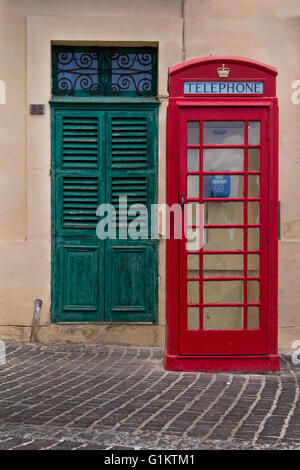 Uno stile tradizionale inglese di un telefono rosso cabina. In sfondo verde antico cancello. Strada del villaggio di pescatori di Marsaxlokk su th Foto Stock
