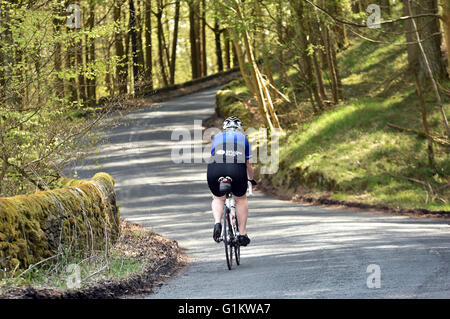 Leggermente sovrappeso ciclista in sella fino alla cima di una collina su un sportivi, Yorkshire Foto Stock