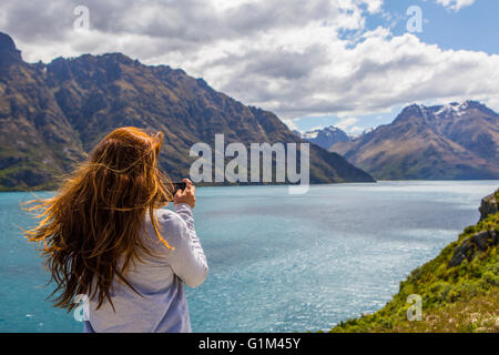 La donna caucasica fotografare montagne e lago, Queenstown, Otago, Nuova Zelanda Foto Stock