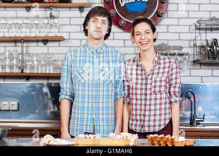 Divertente coppia giovane con farina sui loro volti in piedi e sorridente su la cucina Foto Stock