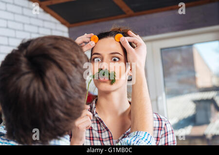 Giocoso coppia giovane divertendosi e rendere divertente volto sulla cucina Foto Stock