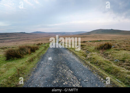 Un solitario paese vicolo che conduce attraverso il tetro brughiera a Okehampton Camp sul Parco Nazionale di Dartmoor in Devon Foto Stock