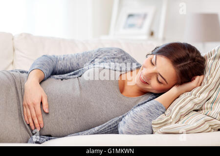 Felice donna incinta sdraiato sul divano di casa Foto Stock