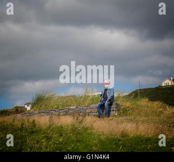 Senior uomo seduto lungo il muro di pietra a Inchydoney spiaggia vicino Clonakilty, County Cork, Repubblica di Irlanda. Eire. Foto Stock