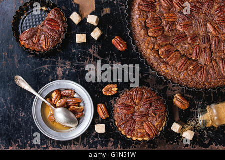 In casa grande caramel torta alle noci pecan e piccole tortine in ferro nero forme, serviti con lo zucchero di canna, la salsa di caramello e vintage Foto Stock