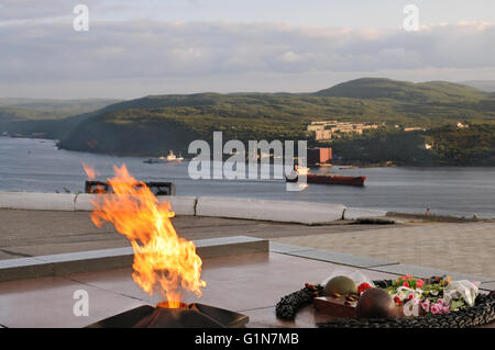 La fiamma eterna accesa sopra la baia di Kola e una nave passando da, a Murmansk, Russia Foto Stock