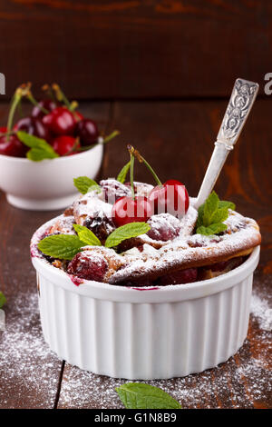 Clafoutis francese con la ciliegia in ceramica ramekins su tavola in legno rustico Foto Stock