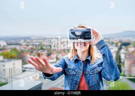 Donna che indossa la realtà virtuale gli occhiali di protezione in piedi su un balcone Foto Stock